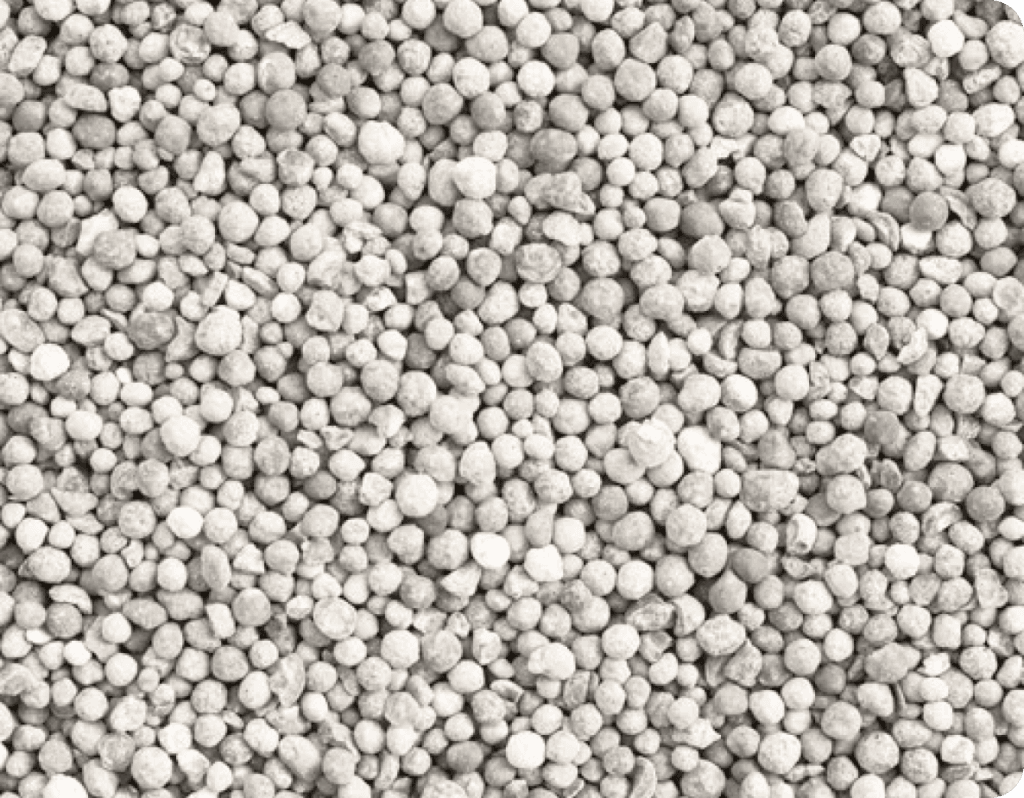 Eine Nahaufnahme von kleinen, grauen Düngemittelpellets, die gleichmäßig auf dem Boden verteilt sind.