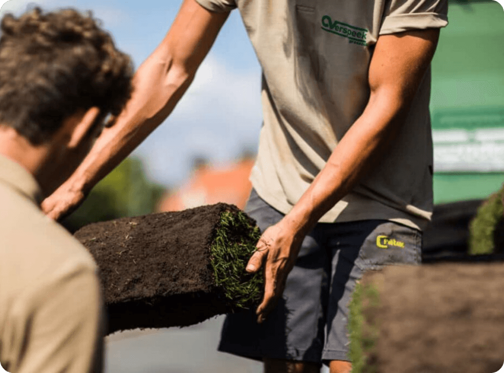 Ein Rasenprofi hält eine Rolle Rollrasen in den Händen. Er kann sie verladen, damit sie der Kunde mitnehmen kann.