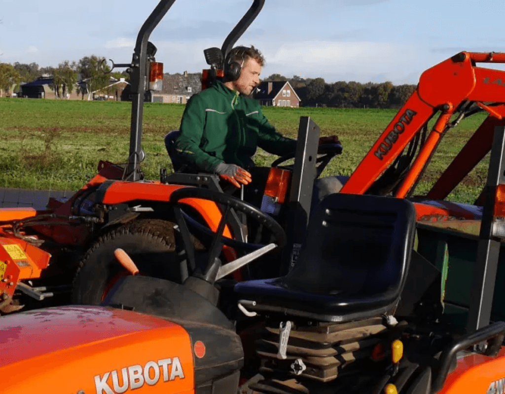 Ein Rasenprofi steuert einen Kleintraktor auf einem Feld. Ein weiterer Traktor ist zusehen.