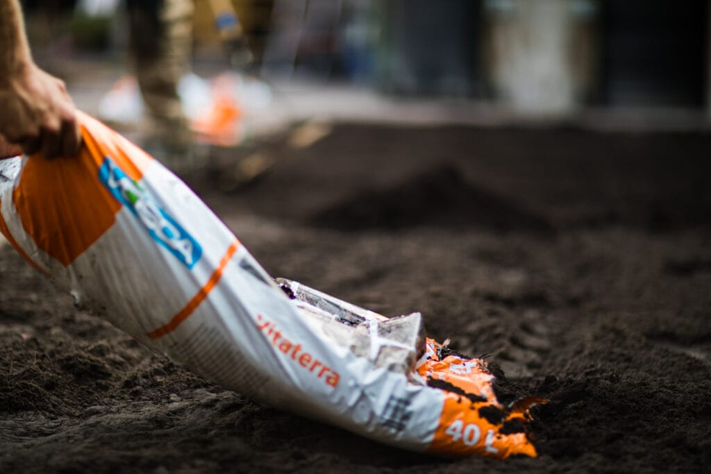 Nahaufnahme eines Arbeiters, der einen Sack mit Erde aufreißt, um ihn in den Boden zu verteilen.