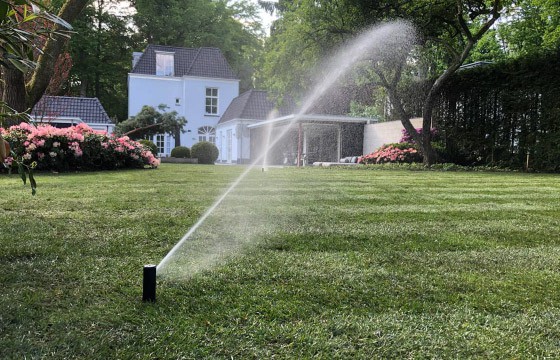 Zwei Rasensprenger bewässern den Rollrasen eines sehr gepflegten Gartens mit Sträuchern und Bäumen