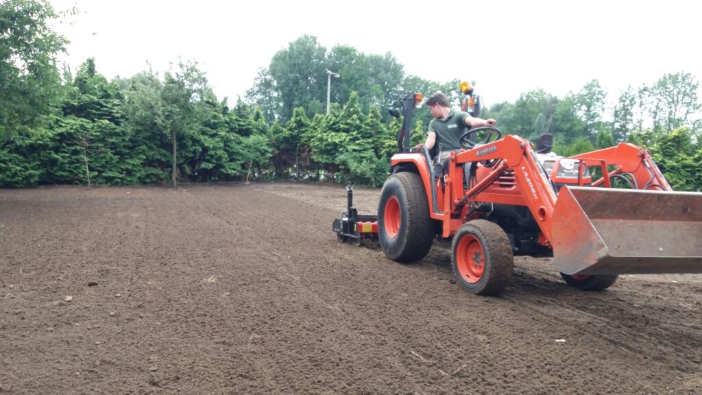 Traktor mit Rotoregge lockert und ebnet den Boden zur Vorbereitung auf die Rollrasenverlegung. Die feine Bodenbearbeitung sorgt für eine gleichmäßige und durchlässige Oberfläche.
