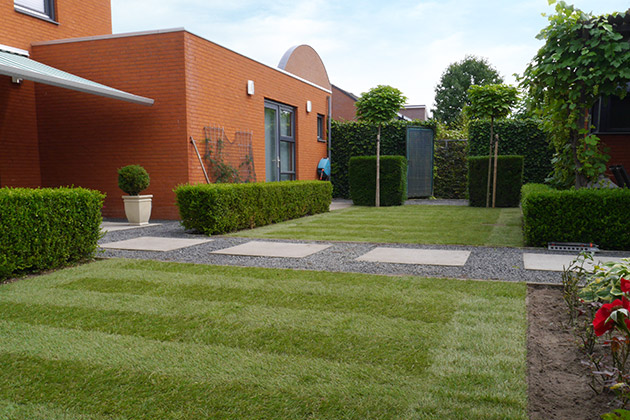Sehr gepflegter Garten mit akkurat geschnittenen Hecken und Sträuchern, mit Rollrasen und einem Weg zu einem Wohnhaus.